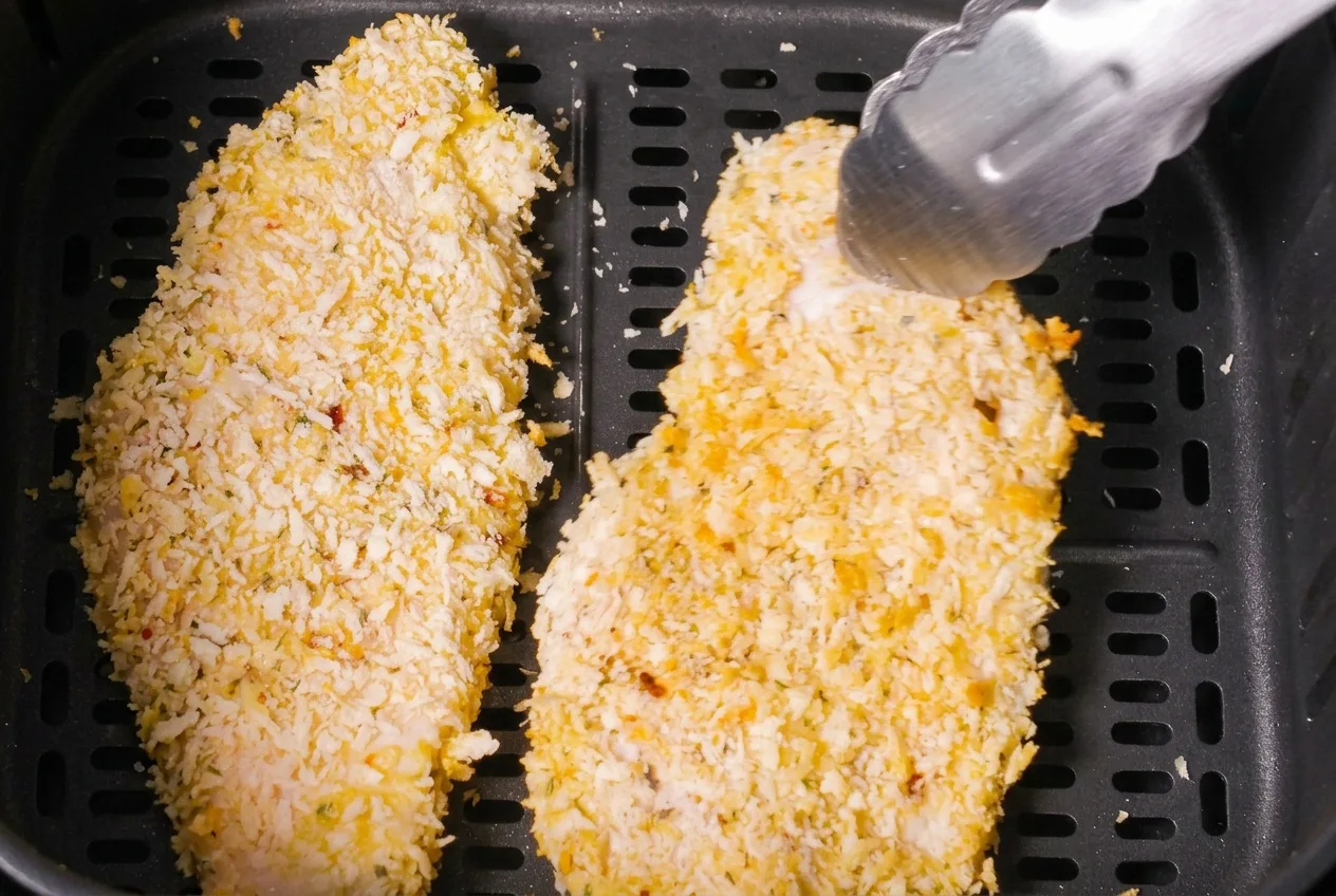 Panko-bundás csirkeszeletek az air fryer rácsán, fogóval