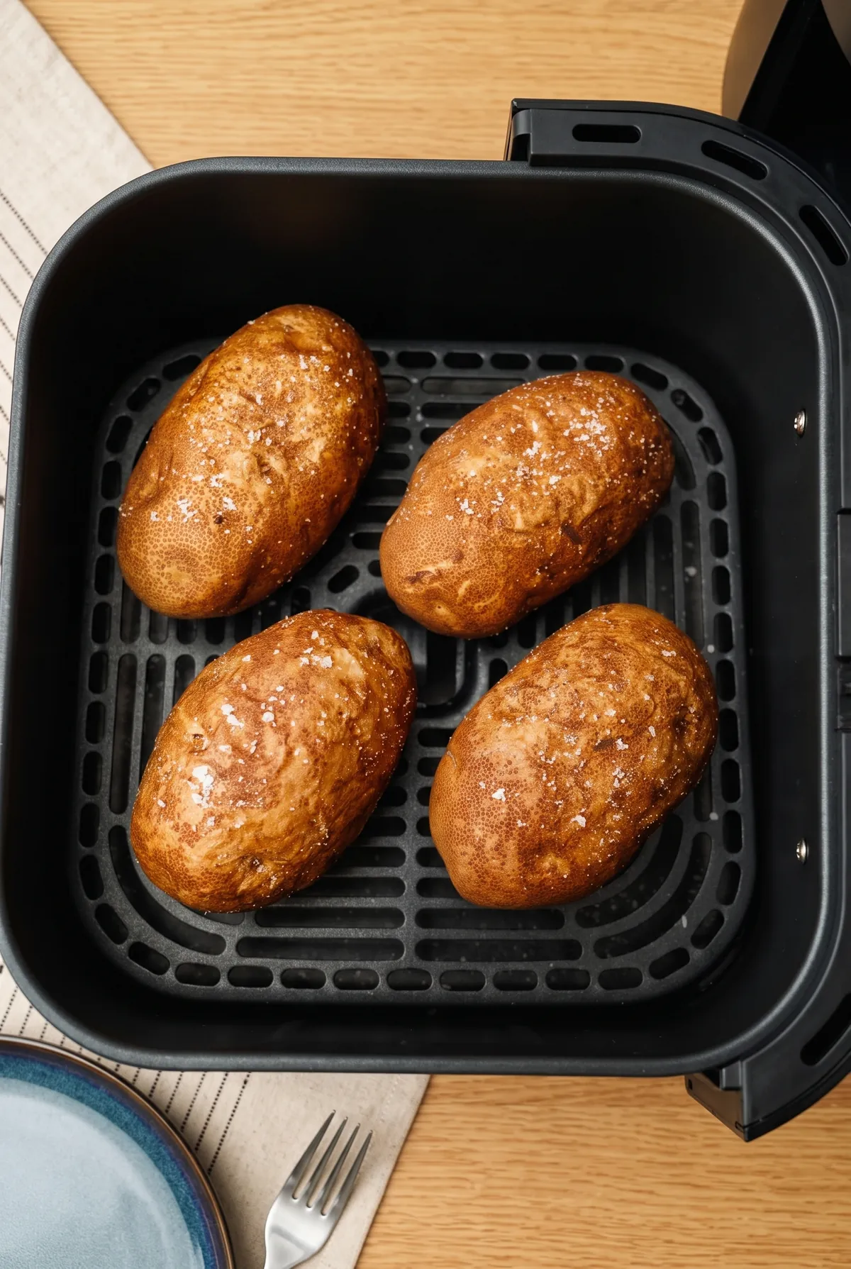 Négy készre sült, ropogós héjú krumpli az air fryer kosarában, sóval megszórva