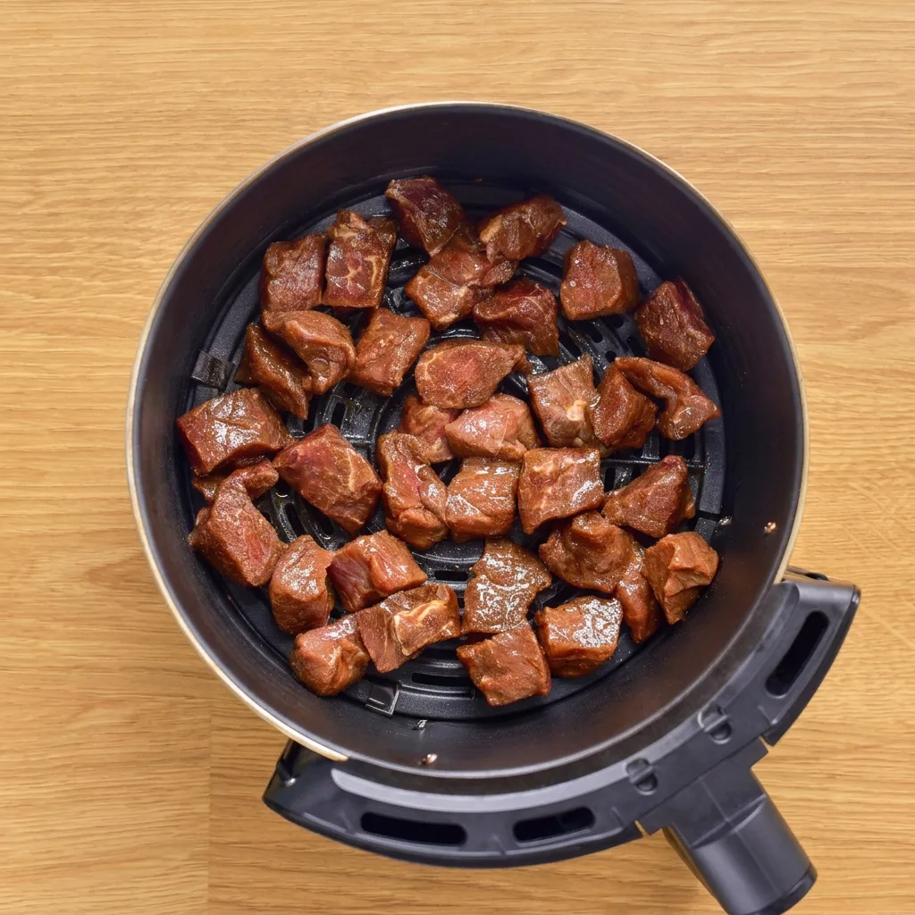 Megsült steakfalatok a kerek air fryer kosárban, felülnézetből